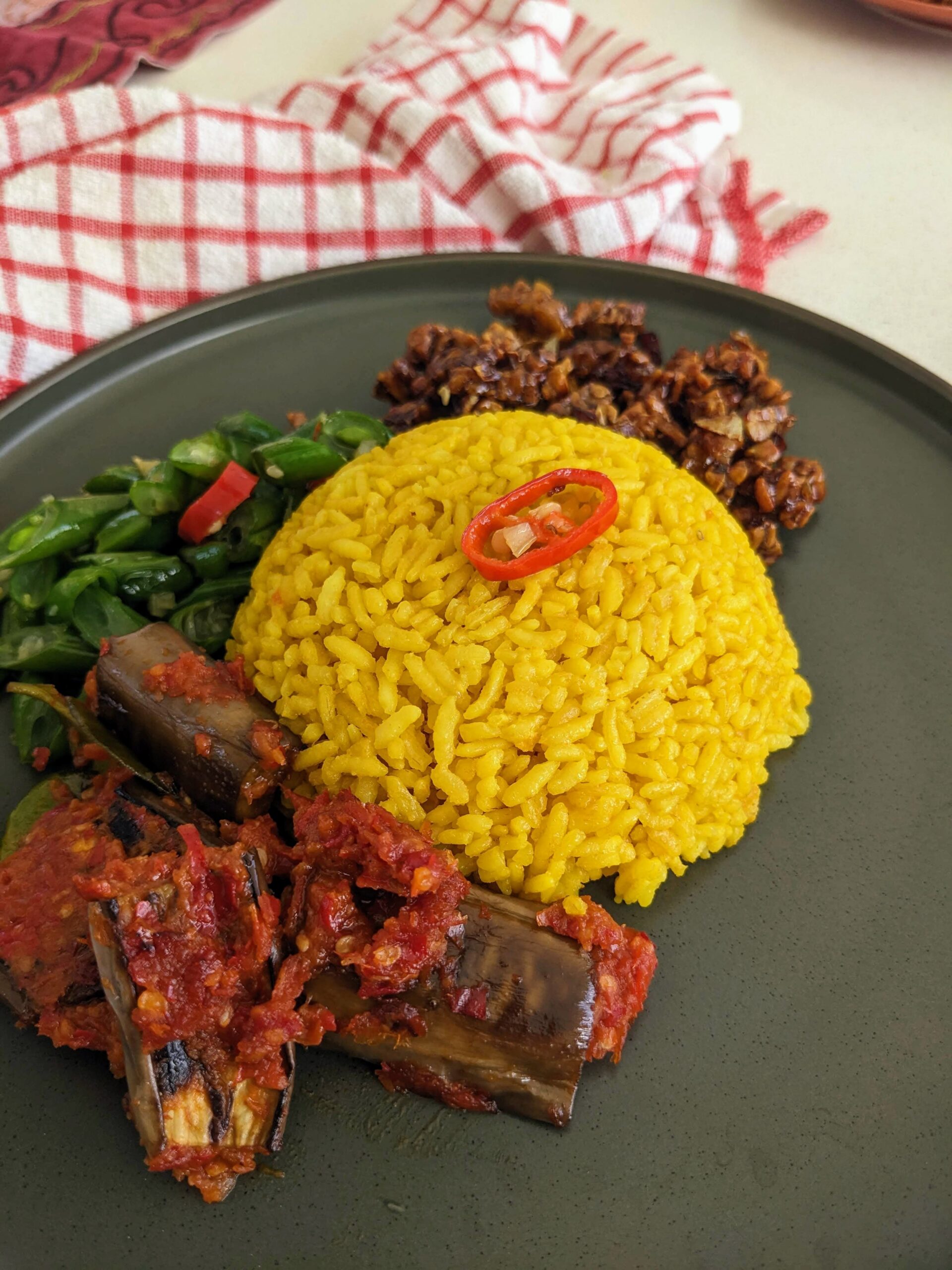 Nasi kuning disajikan dengan lauk tempe orek, terong balado dan tumis buncis