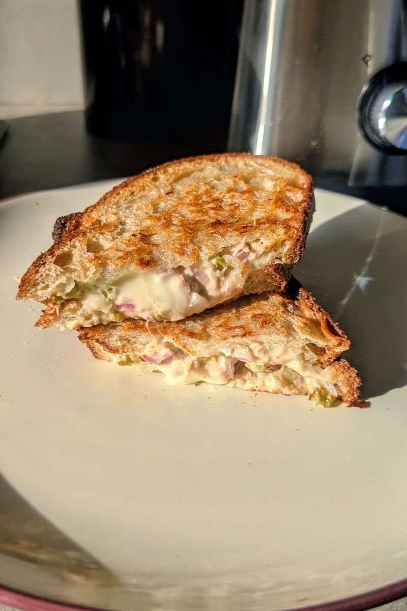 Tuna melt yang sudah di potong menjadi dua bagian bertumpuk disajikan diatas piring
