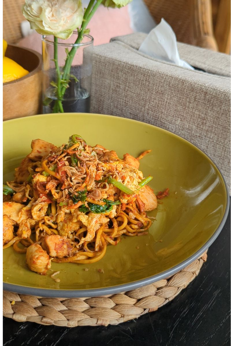 Sepiring mie goreng disajikan dengan berbagai jenis topi seperti ayam, sawi hijau dan wortel. dan ditaburi dengan bawang goreng