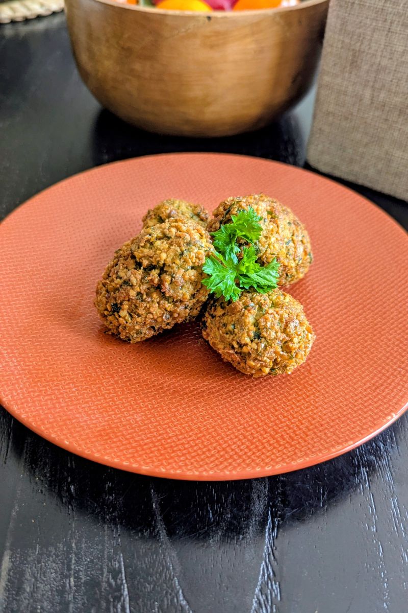 empat buah falafel disajikan diatas piring berwarna oranye dengan parsley sebagai garnish diatasnya